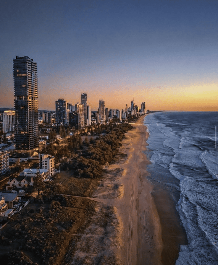 An aerial photo of the city of gold coast with a orange sun setting in the back ground