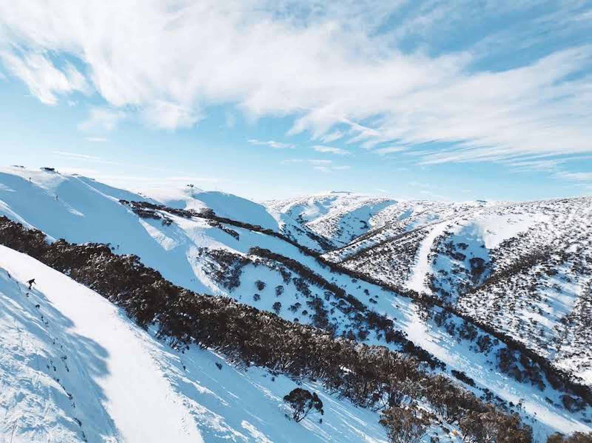 Mount Hotham Australian ski resort. Mountain side is blanketed in white snow. Ski runs are carved between snow gums on the mountain side