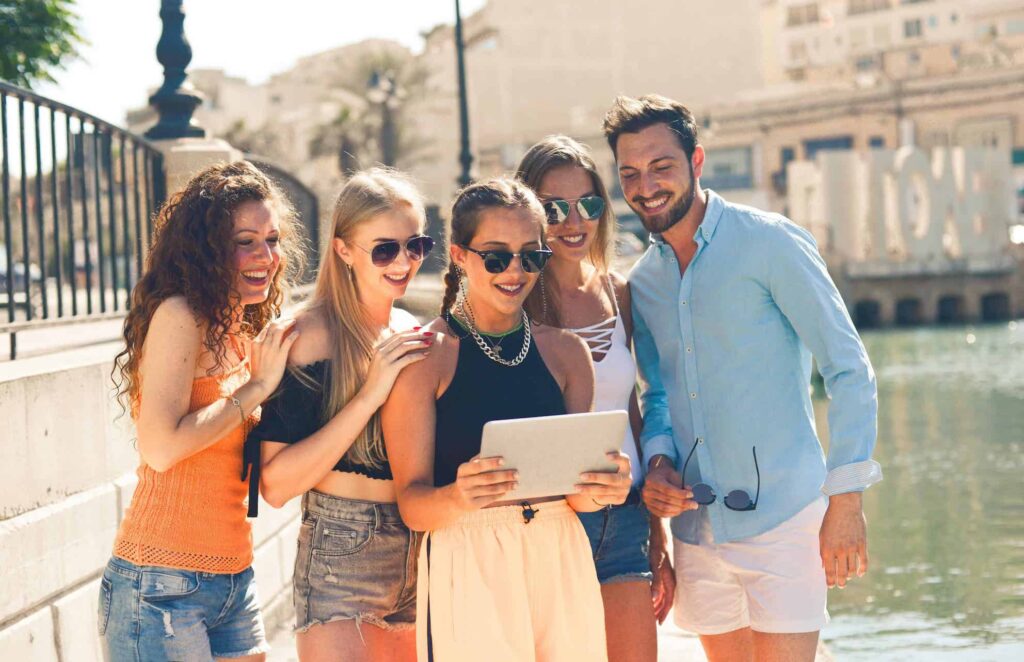 A group of people that met on Travello. 5 people standing next to a river in a city are looking at an ipad.